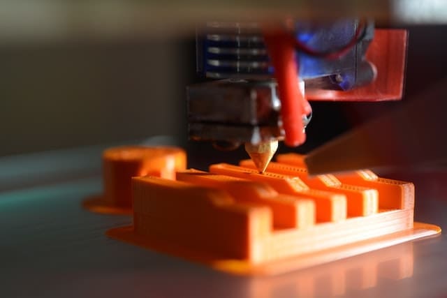 3D printer nozzle printing an out orange filament.